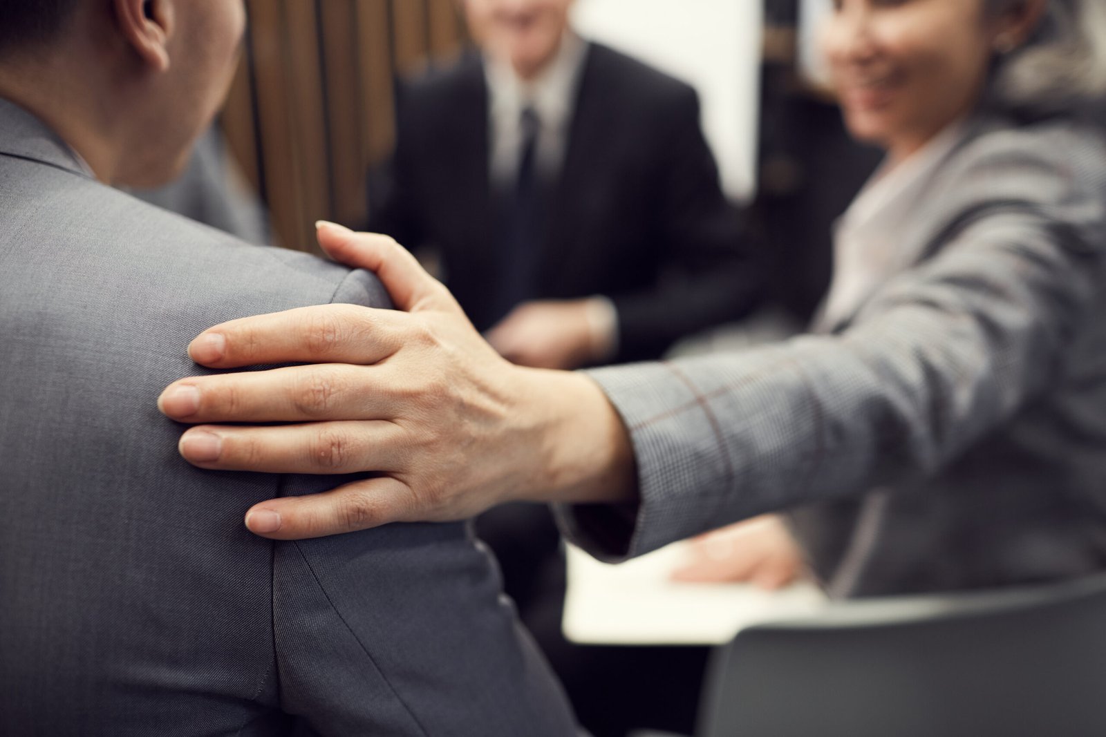 Close-up of business lady touching shoulder of colleague while giving support to him at group business meeting